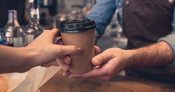 a coffee shop staff handing a cup of coffee to a customer at the counter in togo disposable cup