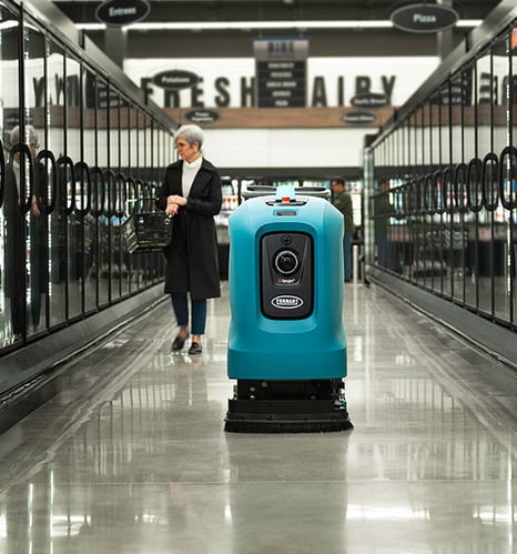 A female customer shopping at the grocery store while autonomous X4 ROVR is cleaning the floor 