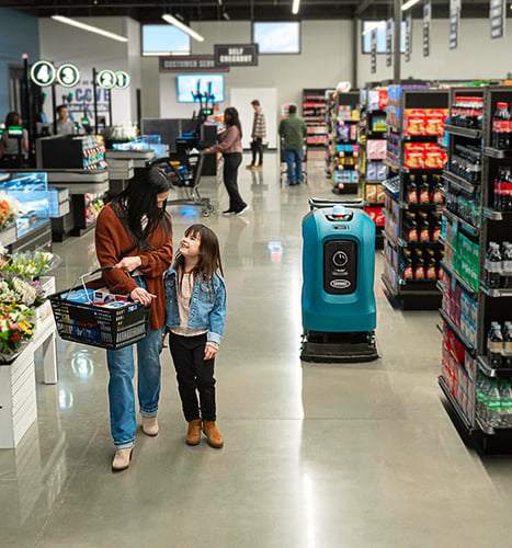 a mom and daughter shopping at the grocery store where autonomous X4 ROVR is cleaning the floor