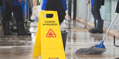 cleaning crew cleaning floor with yellow cleaning in progress sign 