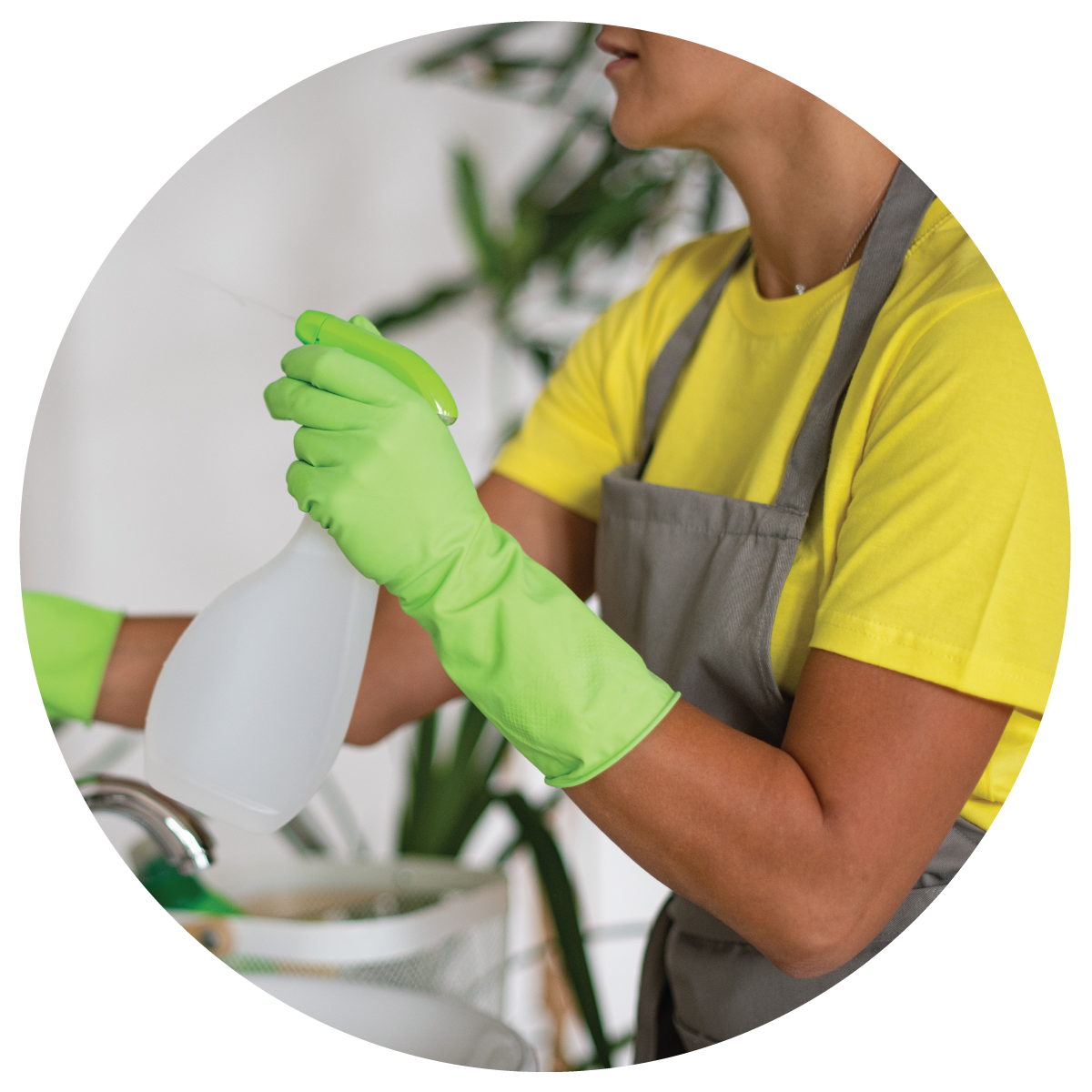 A female janitor cleaning restroom mirror with chemical cleaner wearing light green rubber gloves and gray apron