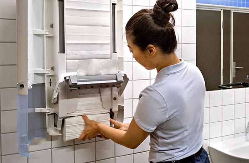 a female custodian refilling paper towels on Tork PeakServe dispenser